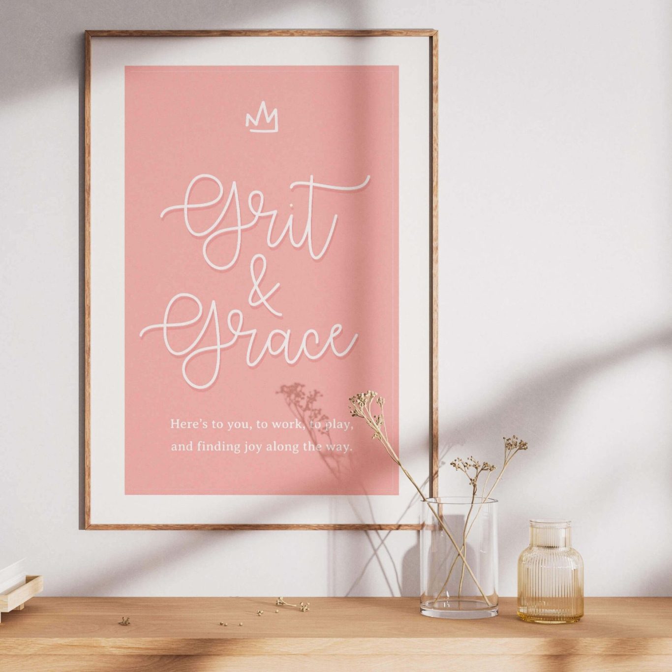 A pink framed poster with the text "Gratitude & Grace" on a shelf with decorative items.